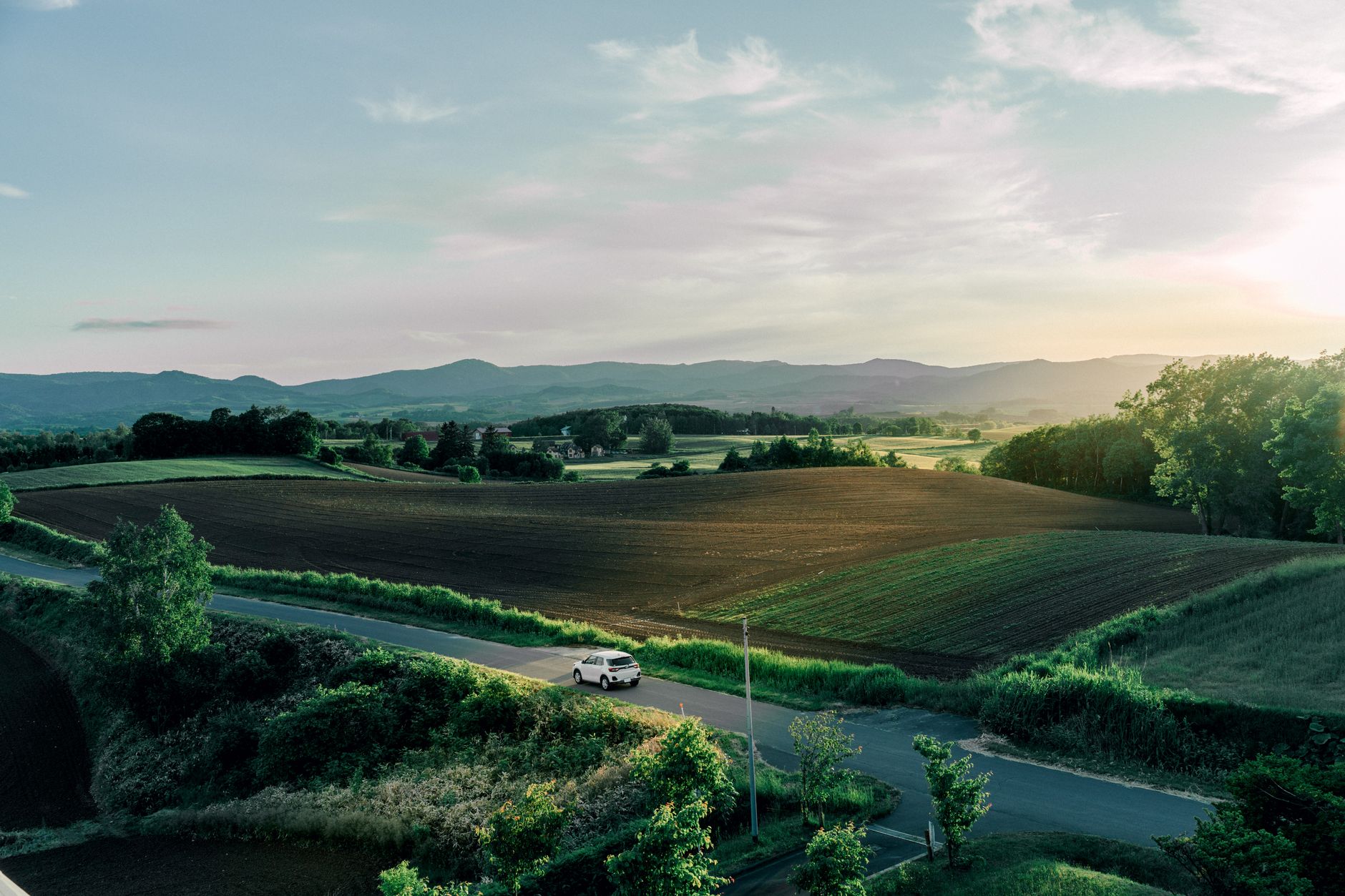 Tranquil rural landscape in Hokkaido, Japan with a winding road, fields, and sunset horizon.
