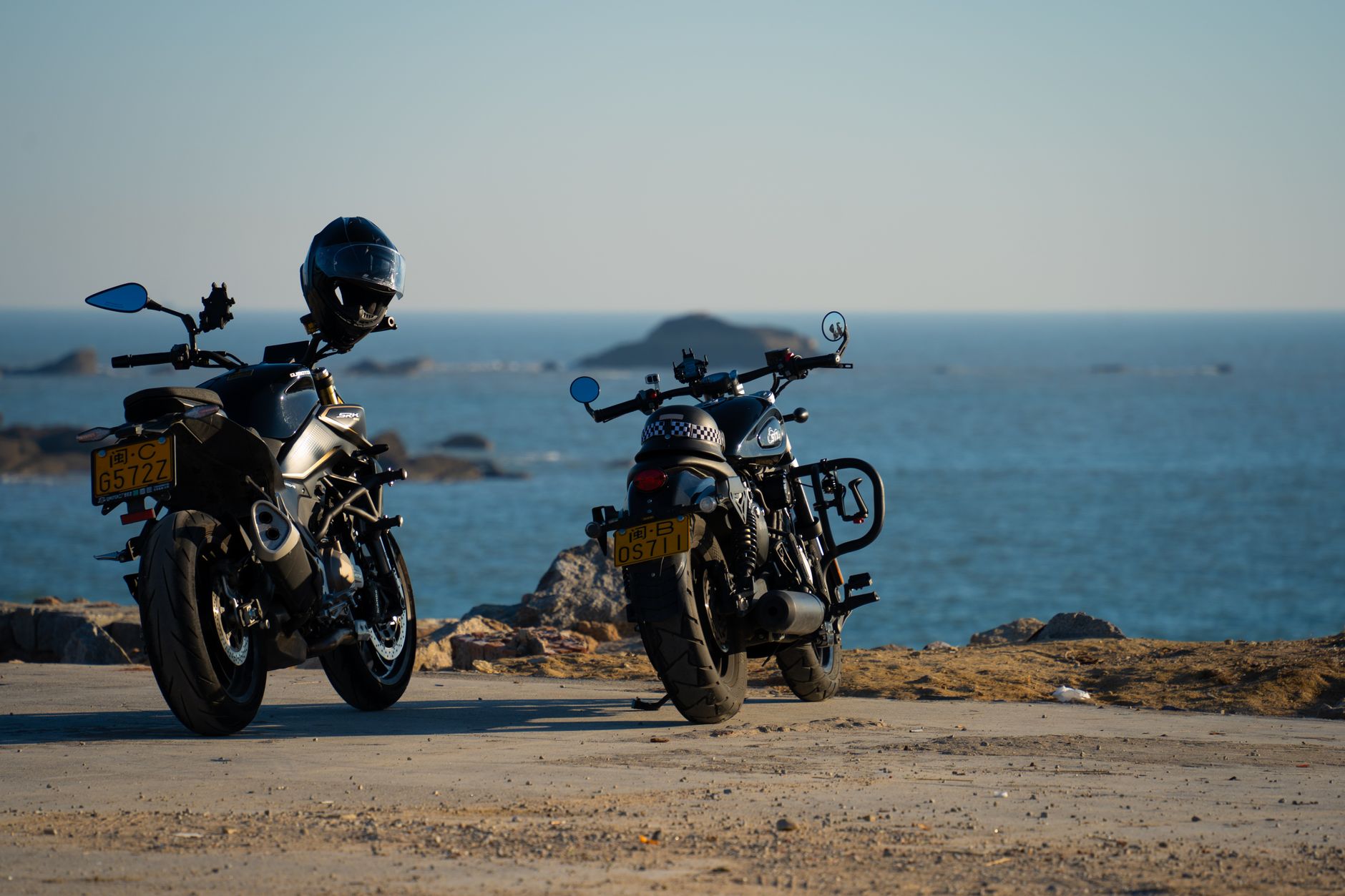 Two motorcycles parked by the ocean with a distant horizon and clear sky.