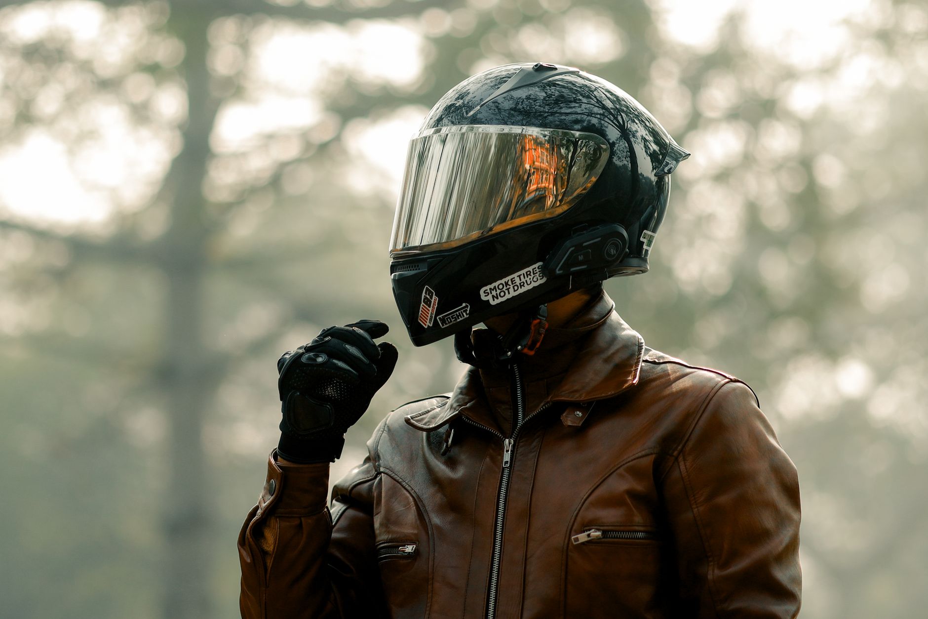 Biker wearing helmet and leather jacket in a foggy forest, evoking adventure.