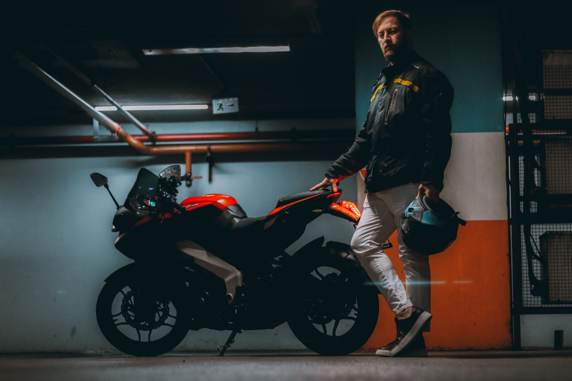 A man holds a helmet beside his motorcycle in a dimly lit garage.