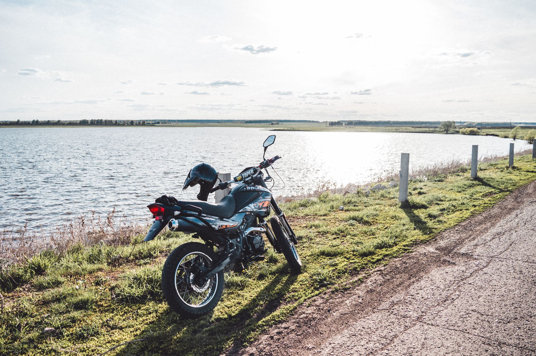 A motorcycle parked on a scenic lakeside road in Bashkortostan, Russia, under a clear sky.