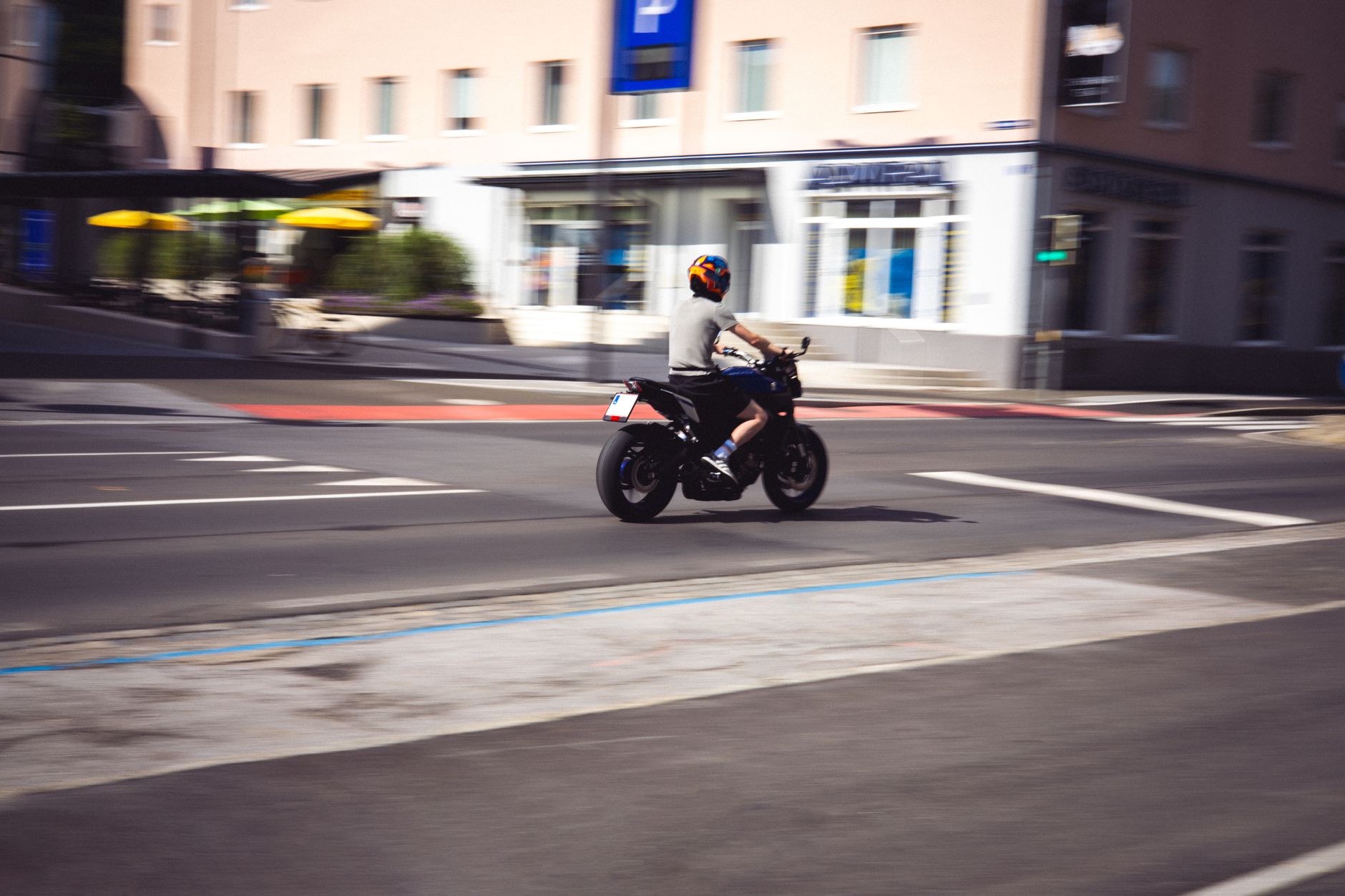 A person on a motorbike rides through a city street in broad daylight.