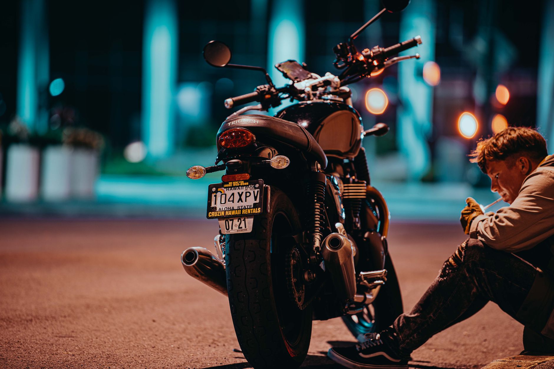 A person smoking beside a motorcycle in an urban setting at night.