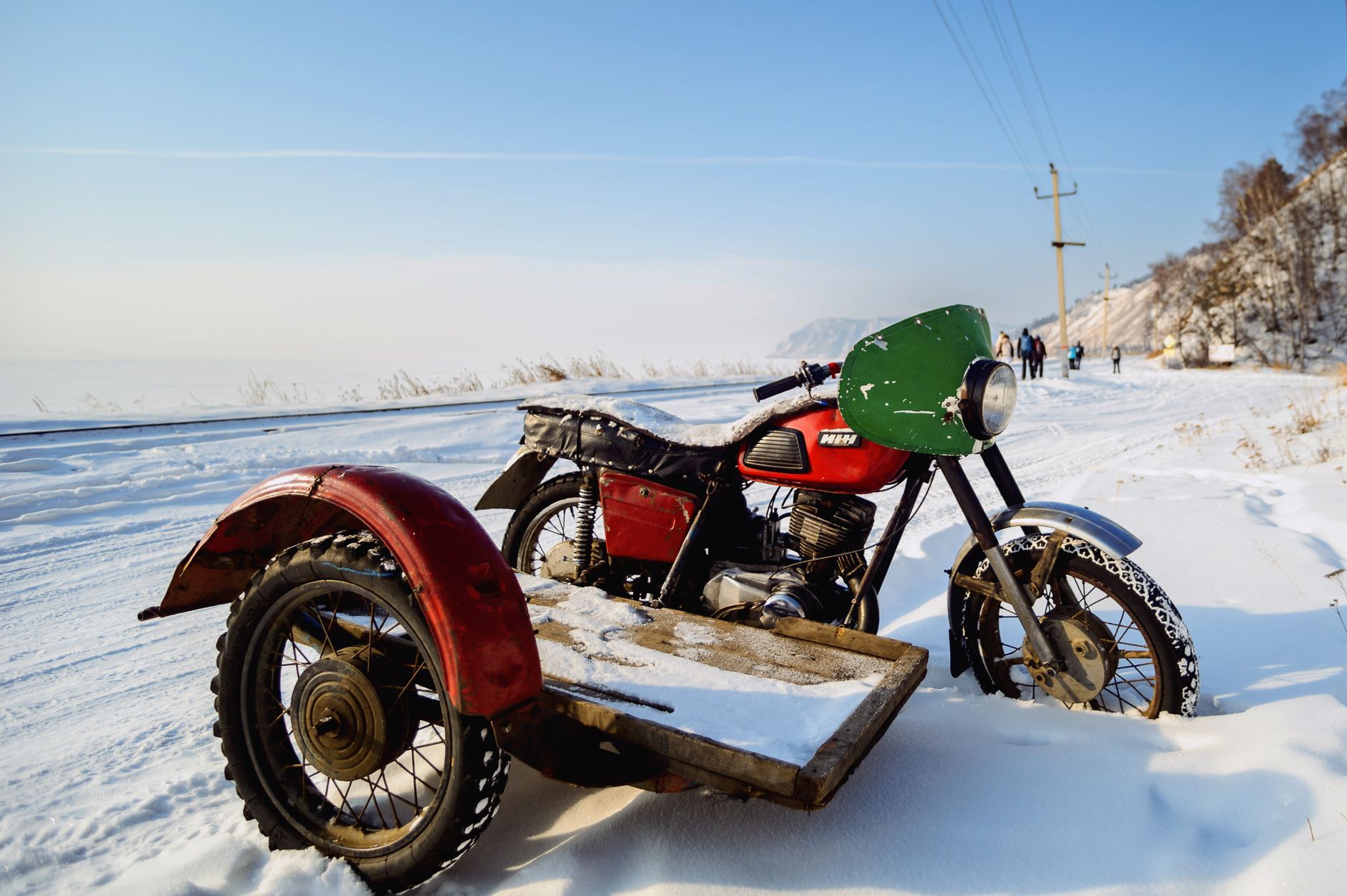 Red and green vintage motorcycle with sidecar parked on snowy road during winter.