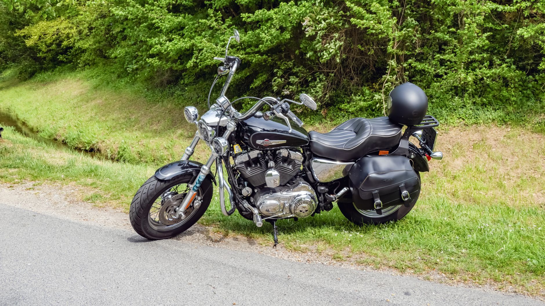 A vintage motorcycle parked by a green roadside in springtime.