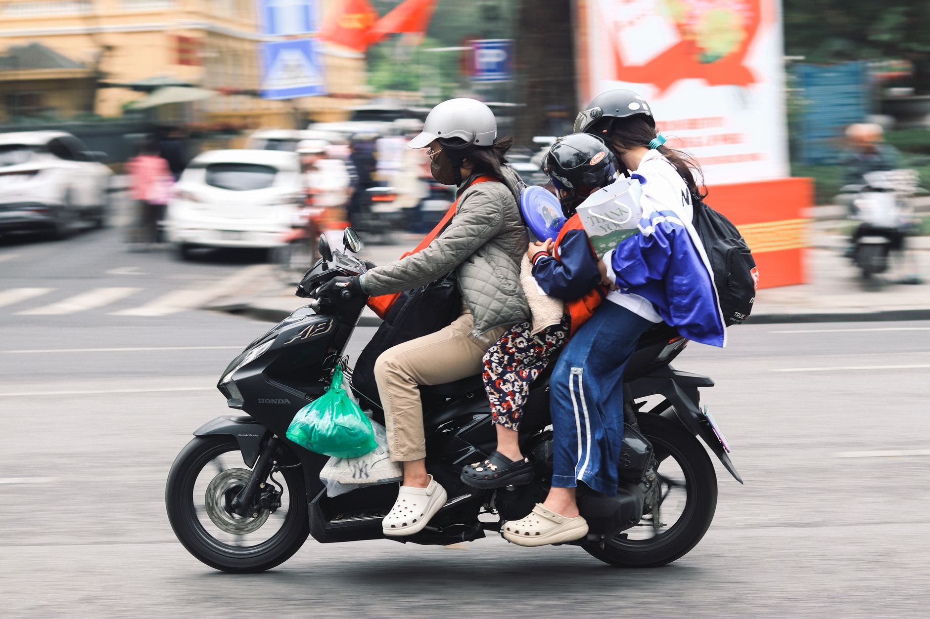 A family of four travels on a motorbike down a lively urban street, demonstrating local transportation methods.