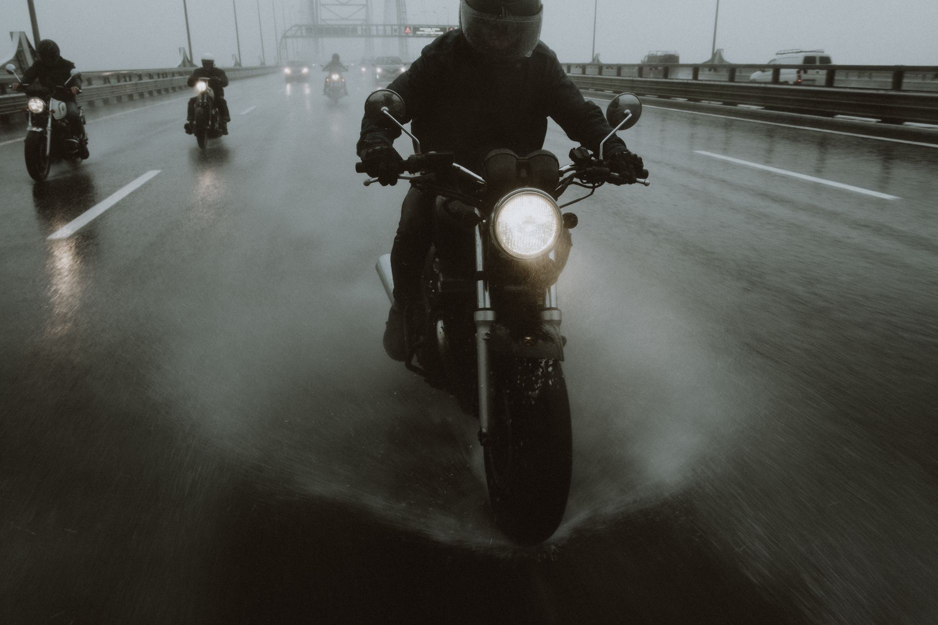 Group of motorcyclists riding in the rain on a highway, creating dynamic splashes.