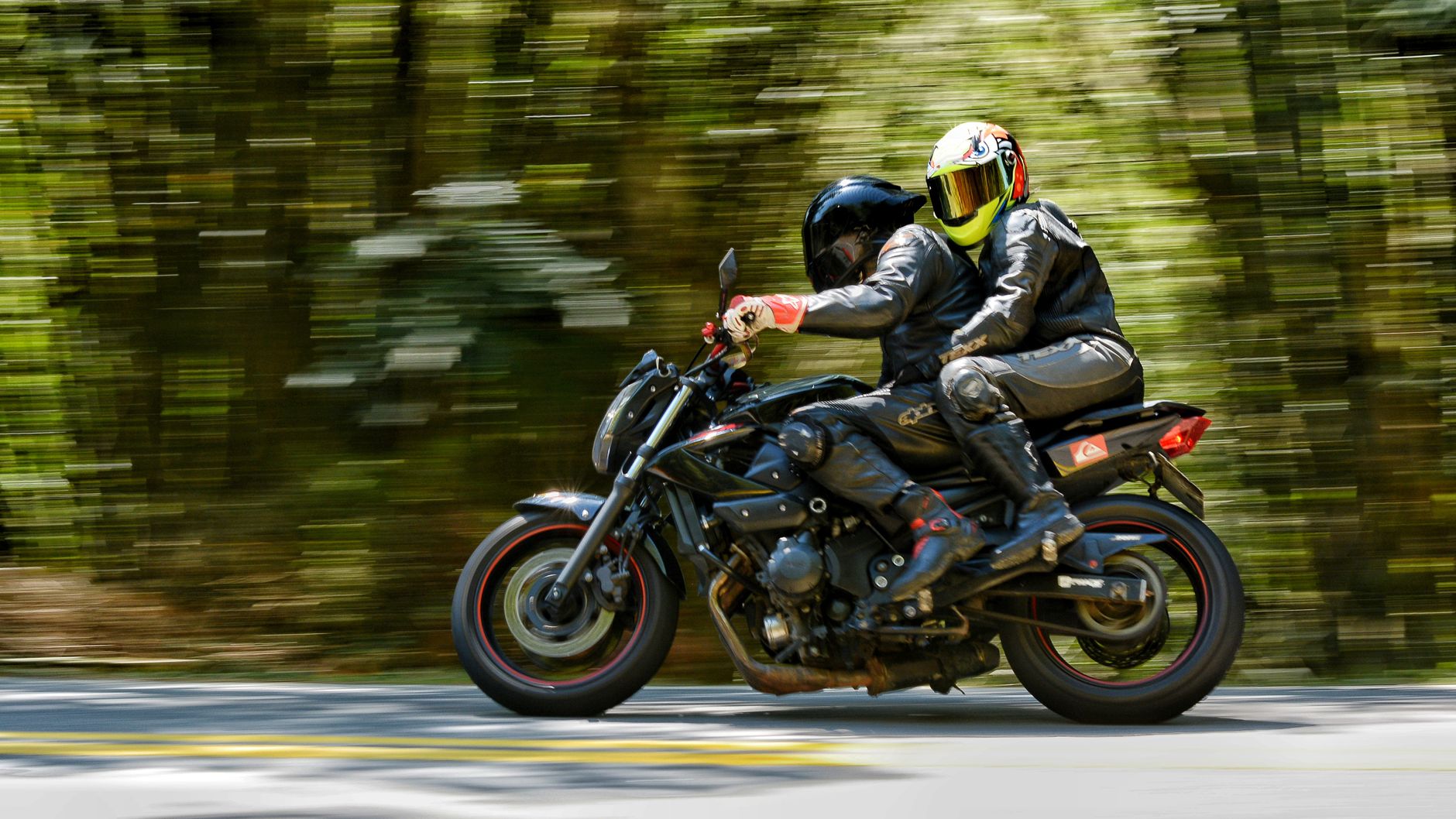 Two motorcyclists speed through a forest road, capturing a sense of thrill and adventure.