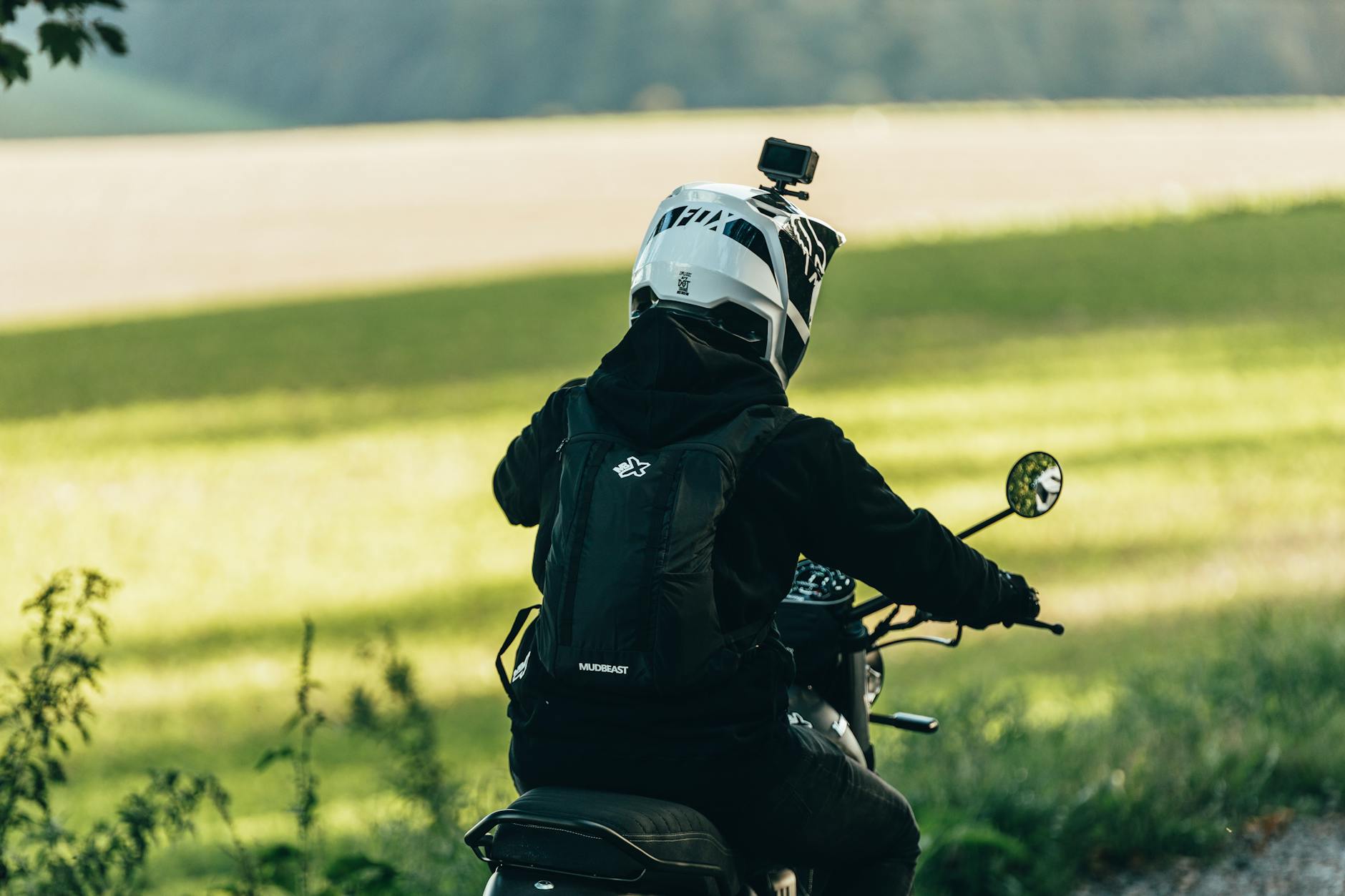 Back view of a motorcyclist wearing helmet and gear traversing a lush countryside road.