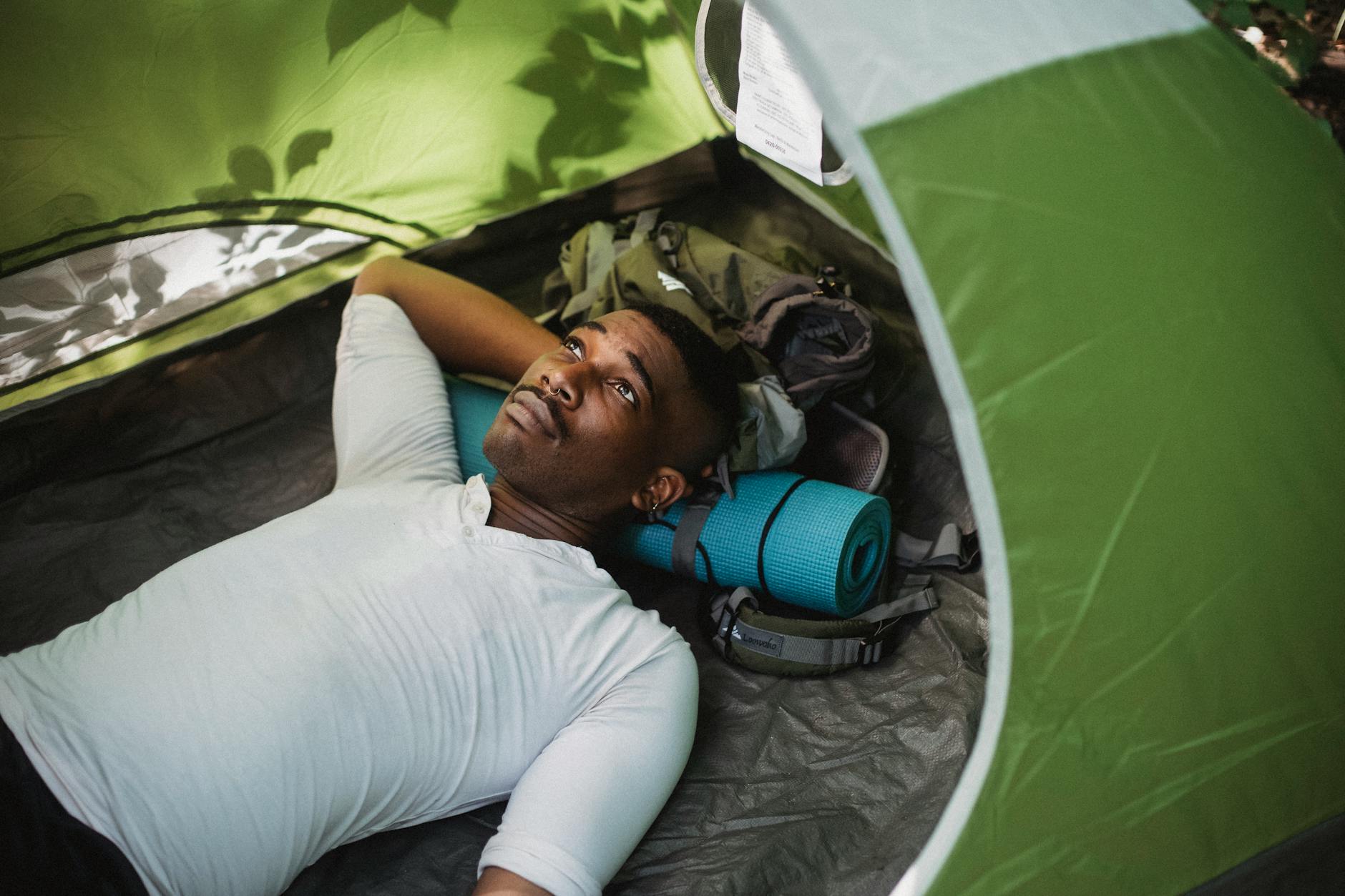 From above of peaceful African American male lying in tent while having break in trekking in nature