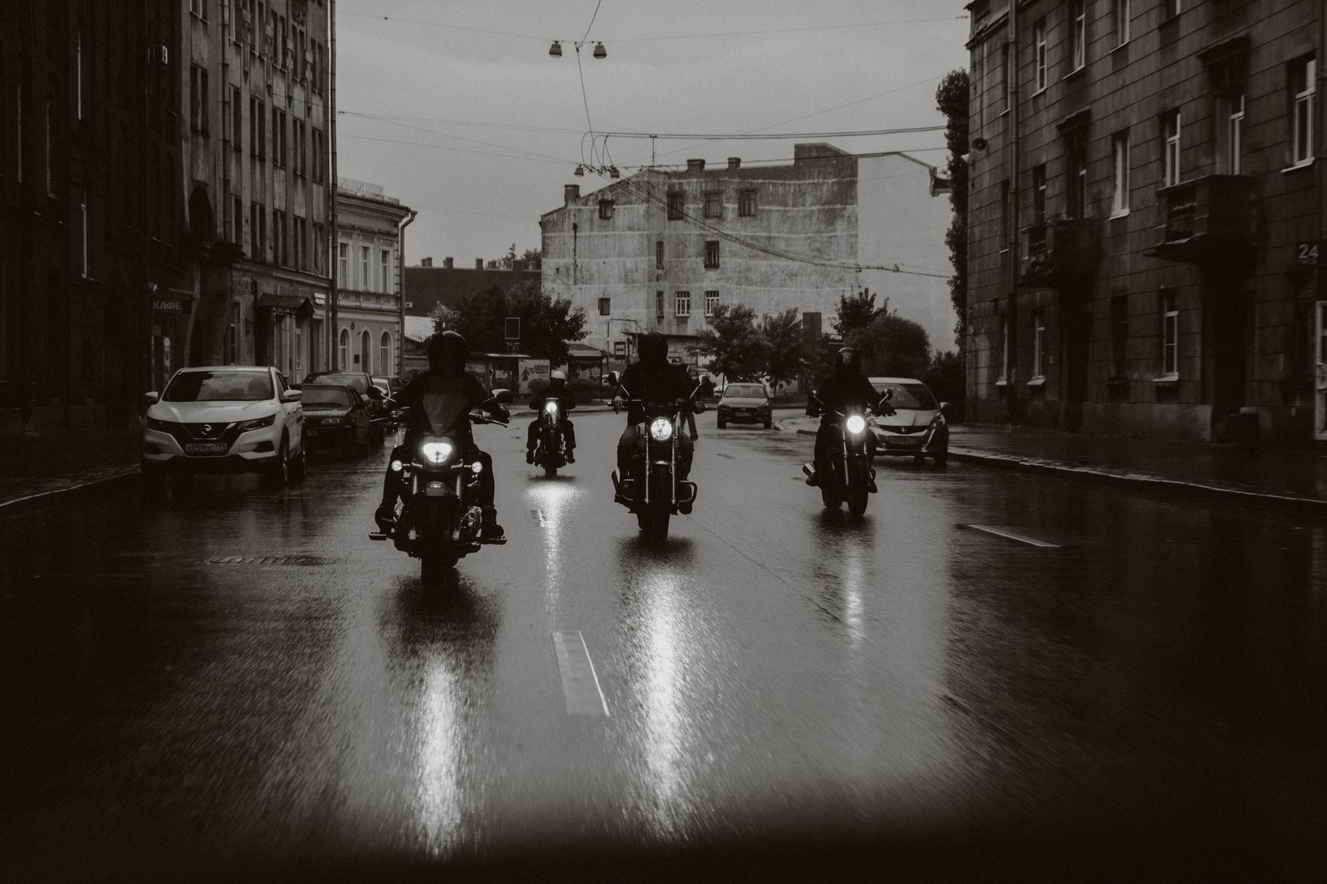 A group of bikers riding through a rainy city street at night.