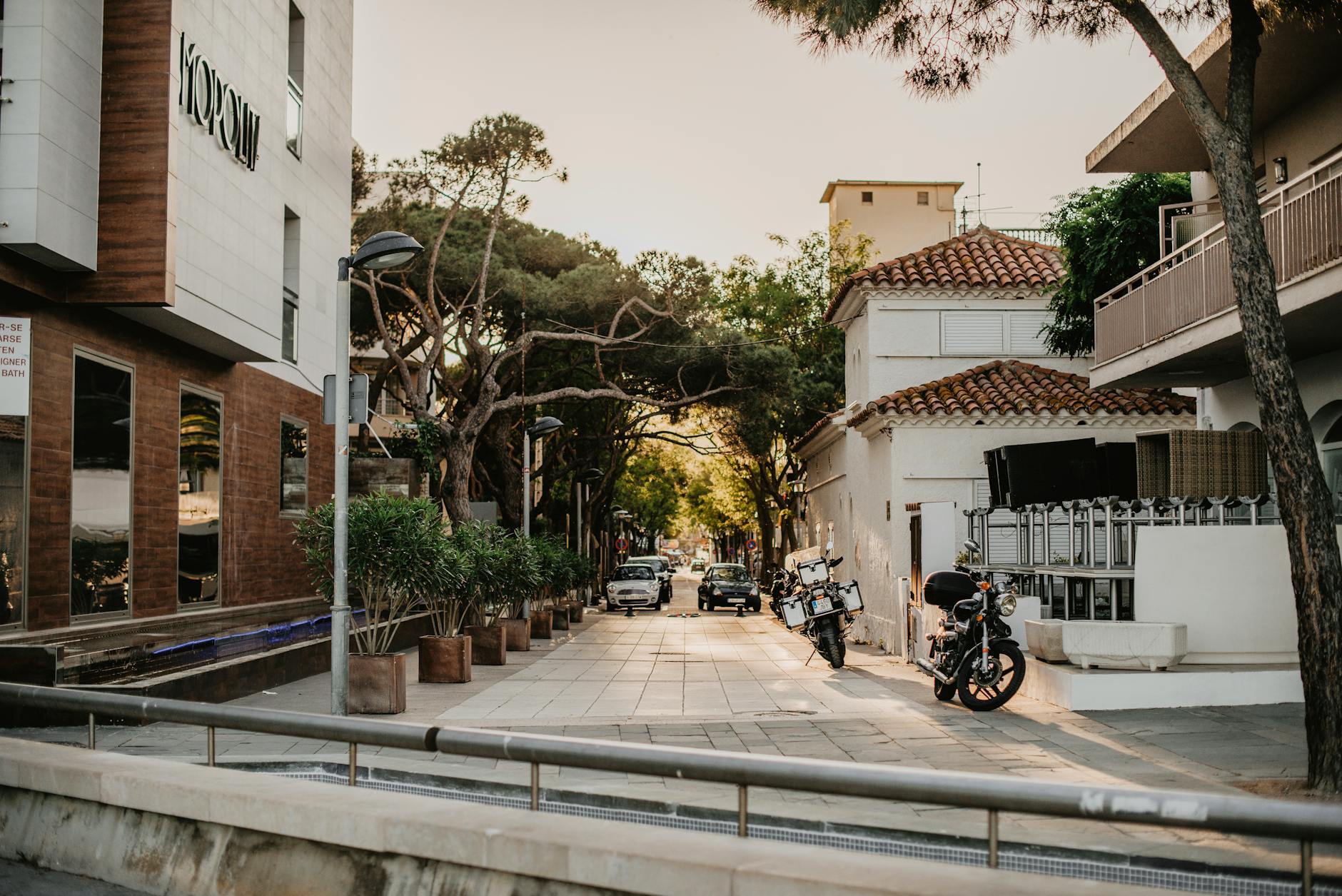 A tranquil urban street scene with motorcycles, lush greenery, and charming architecture at sunset.