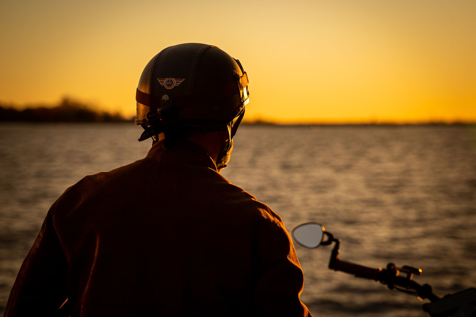 A motorcycle rider enjoys a tranquil sunset by the ocean, embracing the freedom of travel.