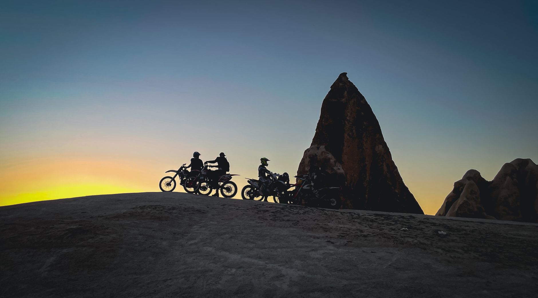 Silhouette of motorcyclists paused against dramatic rock formations at sunset, capturing a sense of adventure.