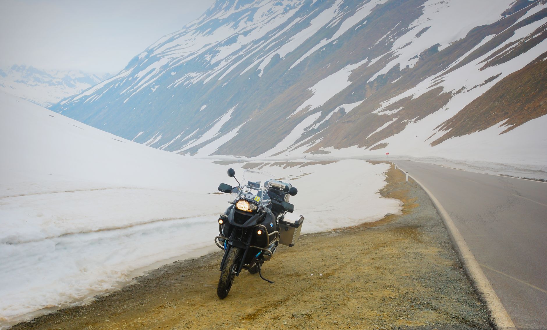 Adventure motorcycle parked by snowy mountain road, evoking exploration and freedom.