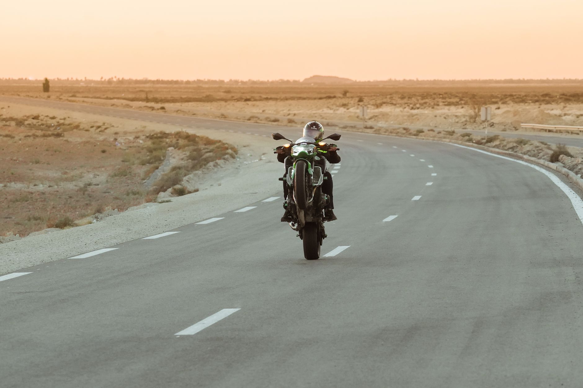 Motorcyclist doing a wheelie on a deserted highway, showcasing skill and thrill.