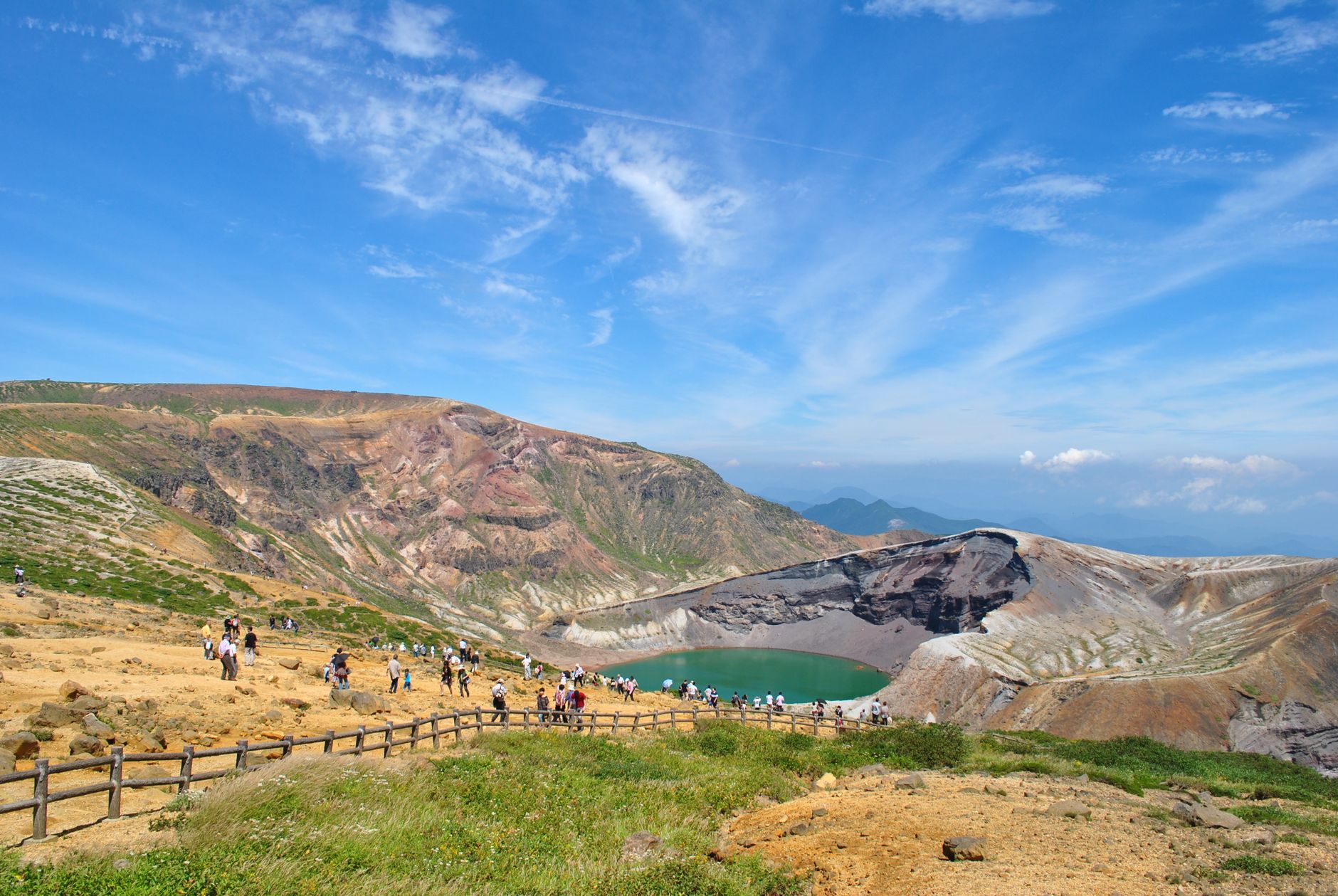 Scenic view of tourists at Okama Crater Lake, Yamagata, Japan, with vibrant landscape and clear blue sky.