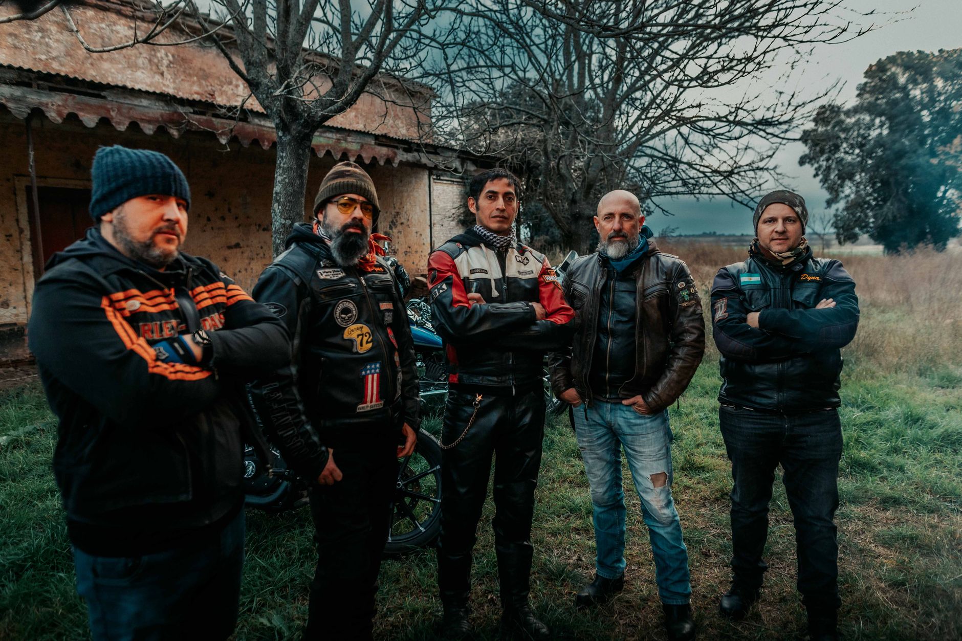 Five men in leather jackets posing outdoors, showcasing motorcycle club camaraderie.
