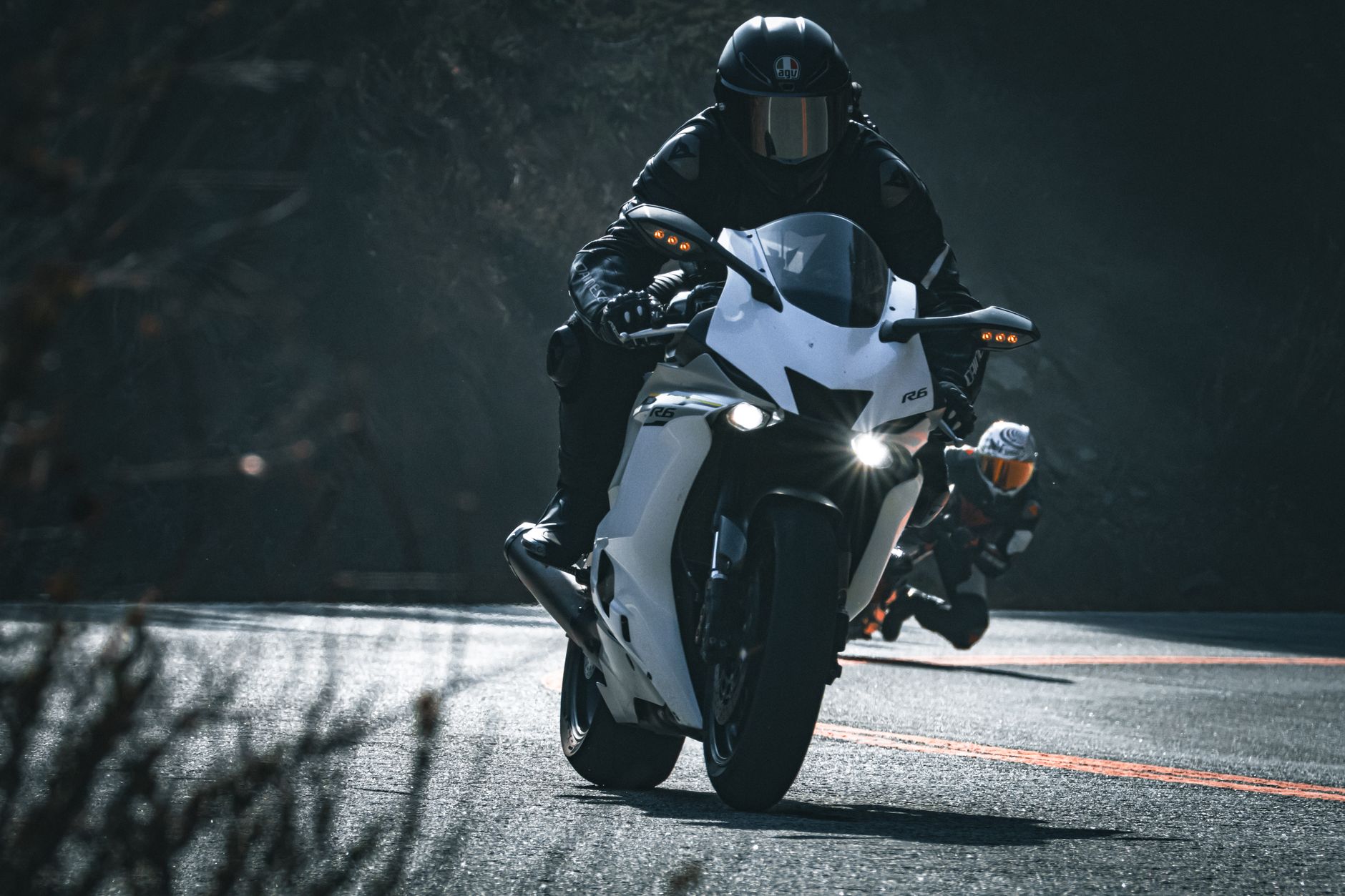 Two motorcyclists racing on a scenic curved road, showcasing speed and precision.
