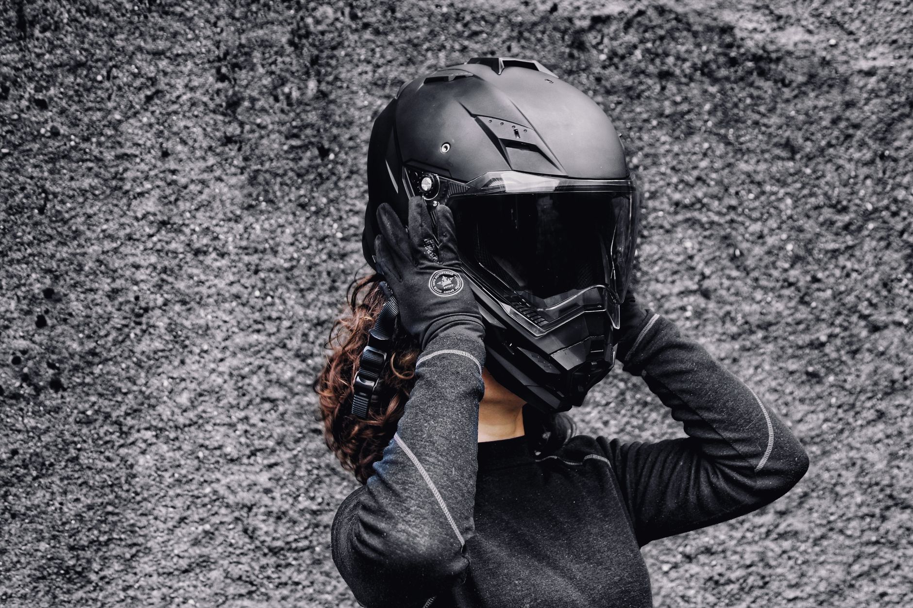 A woman in gloves putting on a motorcycle helmet against a textured background, highlighting safety and adventure.