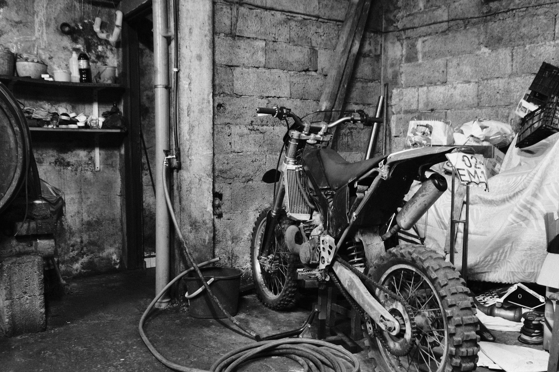 Monochrome image of a dirt bike stored in an old garage setting.